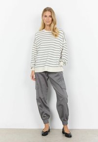 Riba mustriga kreemivärvi suurus sweatshirt hallide joontega, kombineeritud lõdvad hallid cargo püksid elastsete mansettidega ja küljetaskutega. Mustad lamejalatsid.