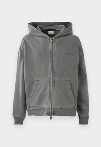 Felpa grigia con zip presenta un ampio cappuccio, tasche frontali e dettagli con logo ricamato. Realizzata in morbido tessuto strutturato con polsini a costine.