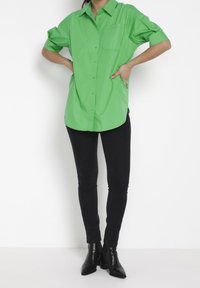 Grön kortärmad skjorta med krage, försedd med en bröstficka. Matchad med svarta skinny jeans och svarta ankelstövlar.