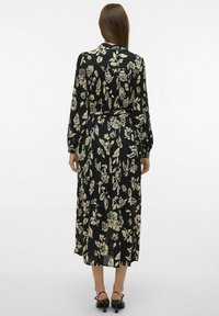 Robe noire à fleurs avec des manches longues, une taille ceinturée et un design plissé agrémenté de motifs floraux crème.