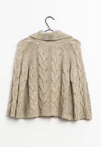 Cardigan en maille beige avec col châle, présentant des motifs torsadés et un ourlet côtelé. Suspendu à un crochet noir sur un fond blanc.
