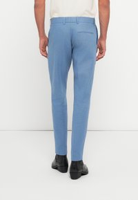 Pantalons ajustés bleu clair, confectionnés dans un tissu lisse. Ils ont une poche arrière et sont portés avec des bottines noires.
