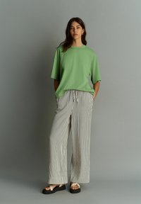 Camiseta verde de gran tamaño con mangas cortas, combinada con pantalones anchos de rayas blancas y negras. Sandalias con suela negra gruesa.