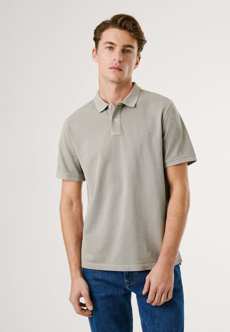 Polo shirt gris clair à manches courtes, col boutonné et logo discret ; associé à un jean en denim bleu. Tissu doux et texturé.