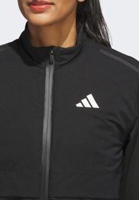 Black athletic jacket with a high collar, full zipper, and a white Adidas logo. Features a smooth texture and subtle reflective accents.