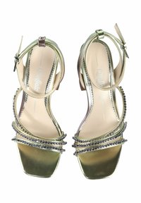 Metāliskas zelta augstpapēžu sandeļi ar kvadrātu purngaliem, vairākiem mirdzošiem siksniņām un akmeņiem gar malām.