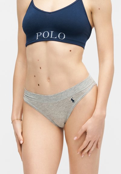 Γυναίκα που φοράει μπλε σκούρο crop top με το κείμενο "POLO" και ανοιχτό γκρι εσώρουχα με μικρό σκοτεινό λογότυπο Polo σε απλό φόντο.