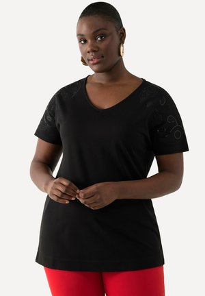 Sort V-hals T-shirt med teksturerede sorte detaljer på skuldrene. Korte ærmer og en afslappet pasform. Båret med røde bukser.