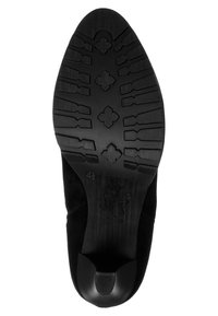 Suela negra con superficie de goma texturizada con un patrón de líneas y formas. Incluye una sección de tacón redondeada y la marca de talla 4½.