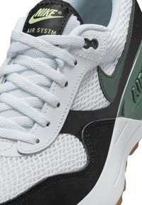 Sneaker Nike Air System con tomaia in rete bianca, accenti in suede nera, marchio verde e suola testurizzata con un design prominente.