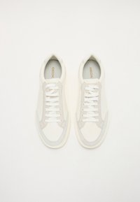 Weiße Leder-Sneaker mit strukturierten Wildlederelementen, flachen Schnürsenkeln, runder Zehenform und einer leicht erhöhten Gummisohle. Das Innere zeigt ein dezentes Markenlogo.