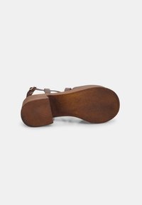 Brown leather sandal with a textured sole, adjustable straps, and a chunky heel. The bottom shows wear and features curved edges.