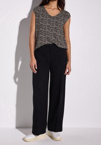 Černé kalhoty se širokými nohavicemi a bočními kapsami v kombinaci s vzorovaným, strakatým topem s výstřihem do V v černé a krémové barvě, který má krátké rukávy.