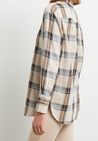 Camicia a quadri beige con strisce blu, nere e marroni; maniche lunghe con polsini a bottone; tasca posteriore singola; orlo curvo.