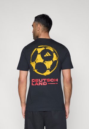 T-shirt en coton noir arborant un grand motif de ballon de football jaune et le texte "DEUTSCHLAND" en rouge vif en lettres majuscules au dos. Design simple avec col rond.