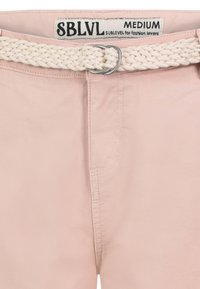 Lichtroze broek met een geweven crèmekleurige riem, zilveren gesp en voorzakken; zachte textuur met zichtbare stikdetails.