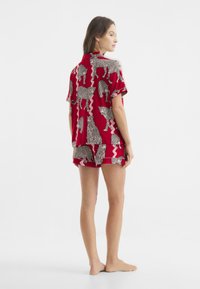 Roter Schlafanzug mit kurzen Ärmeln und Shorts, ausgestattet mit einem schwarzen Leopardenmuster und welligem Design. Hergestellt aus leichtem, glattem Stoff.