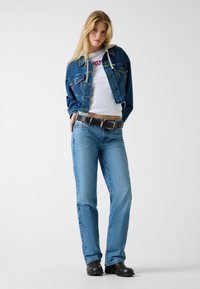 Kurtka dżinsowa w jasnoniebieskim odcieniu, w zestawie z białym, krótkim t-shirtem i prostymi niebieskimi dżinsami. Do kompletu czarny pasek i botki za kostkę.