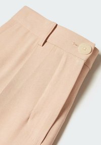 Pantalon rose clair en tissu texturé avec une ceinture lisse, des poches latérales et un bouton rond de couleur crème en accent.