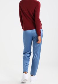 Pull en maille rouge et pantalon en satin bleu clair. La tenue est associée à des baskets blanches, mettant en valeur une coupe décontractée et une texture lisse.