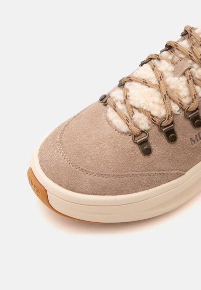 Baskets en daim beige avec doublure en polaire crème, lacets camel et marron, œillets en métal, et une épaisse semelle blanc cassé avec une pointe de bande de roulement marron.