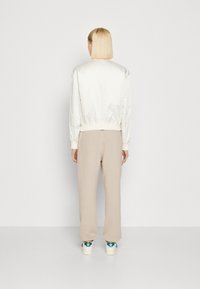 Krémová bomber bunda s žebrovanými manžetami, v kombinaci s béžovými volnými kalhotami. Bílé tenisky s zelenými akcenty na patě.