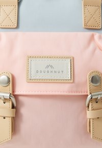 Backpack with a light blue upper section and a pink lower section, featuring beige leather accents and a label marked "DOUGHNUT."
