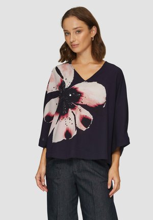 Fließende marineblaue Bluse mit großem pinkfarbenen und schwarzen Blumenmuster, V-Ausschnitt und lockeren Ärmeln, gefertigt aus weichem Stoff mit glatter Textur.