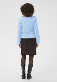 Pull bleu clair et moelleux à manches longues, associé à une jupe en daim brun foncé ajustée. Bottes noires montantes jusqu'aux genoux avec boucles.