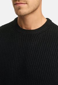 Suéter negro de punto acanalado con cuello redondo, que muestra un patrón texturizado. La tela parece suave y cálida. Sin hardware ni acentos visibles.