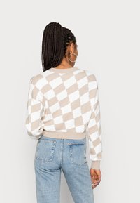 Jersey de punto a rayas beige y blanco con cuello redondo, diseño recortado y puños acanalados, combinado con jeans de color azul claro.