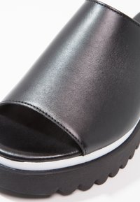Sandale noire à enfiler à plateforme avec large dessus en cuir, bout ouvert, bordure blanche sur une semelle noire épaisse, et semelle extérieure rainurée pour une meilleure adhérence.