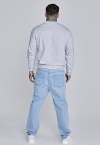 Šedá mikina, světle modré volné džíny a bílé tenisky. Mikina má žebrované manžety a lem, džíny mají zadní kapsy.