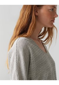 Strickpullover in Grau mit V-Ausschnitt und lockerer Passform. Mit einem Karomuster und weiten Ärmeln, die das Strickmaterial und die Designdetails betonen.