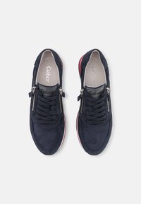 Marinblå mockaskor med snördesign, silverfärgad dragkedja och röda detaljer på sulan. Avtagbar innersula och märkesinnersulor synliga.