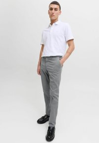 Camisa polo blanca de manga corta y cuello, combinada con pantalones grises claros. El modelo lleva zapatos negros con acentos de borlas.