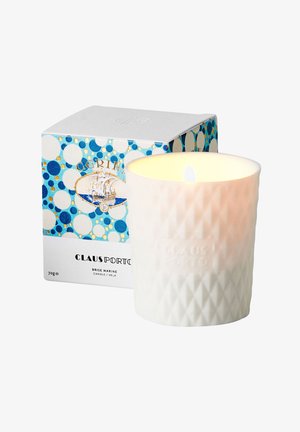 Brennende weiße Kerze mit Struktur in einem mattierten Glasbehälter neben blau-weiß gepunkteter Verpackung mit einer Schiffsillustration und der Marke „Claus Porto“.