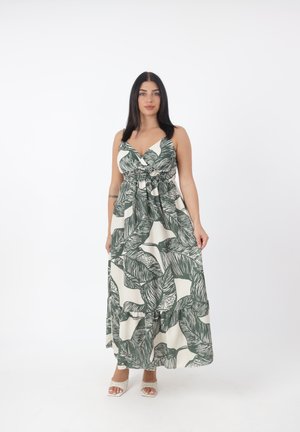 Robe maxi crème avec motif de feuilles vertes, décolleté en V et taille élastique. Présente un ourlet à volants et des bretelles ajustables. Portée avec des sandales.