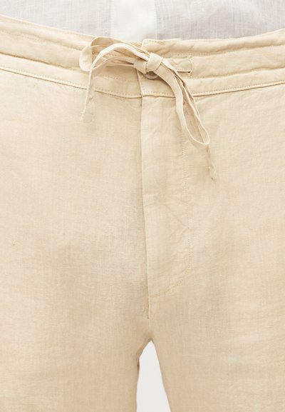Μπεζ λινό παντελόνι με δεμένο υφασμάτινο κορδόνι στη μέση και εμφανείς λεπτομέρειες ραφής.