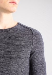 Dark grey knit sweater with a textured surface, round neckline, and raglan sleeves. Features a smooth fit and no visible hardware.