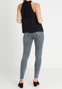 Svart halterneck-top med en fluga vid nacken, tillsammans med åtsittande ljusgrå jeans och svarta klackskor.