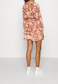 Abito floreale nelle tonalità di rosa e giallo, con maniche lunghe, orlo arricciato e apertura a chiave sul retro, abbinato a sneakers bianche.