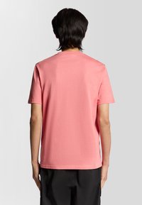 T-shirt a maniche corte in cotone rosa brillante con scollatura rotonda e texture liscia, vista da dietro. Senza motivi o grafiche visibili.