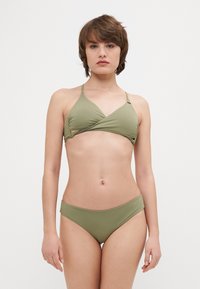 Olíva zöld bikini, amely triánguláris felsőrésszel rendelkezik, keresztezett dizájnnal és állítható pántokkal, alacsony fazonú bikini alsóval párosítva, sima felülettel.