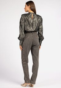 Donker metalen blouse met opgeblazen mouwen en een keyhole achterkant, gecombineerd met hoogsluitende grijze denim broeken. Beige hakken maken de look af.