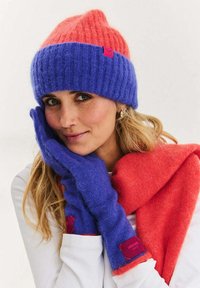 Vícebarevná pletená čepice v růžové a modré barvě s žebrovanou strukturou. K tomu ladící fialové rukavice a červená šála s hladkou strukturou, s označenými detaily.