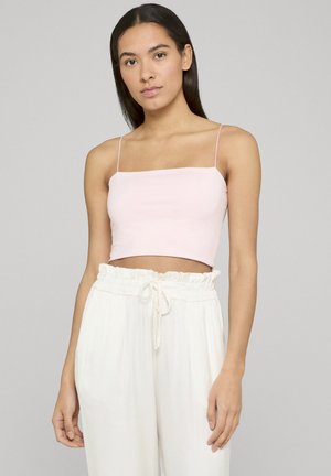 Young woman with long dark hair wearing a light pink cropped spaghetti strap top and high-waisted white drawstring pants.