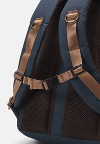 Sininen kangaskärry, jossa on verkkokohdistuksia, pronssiset hihnat ja muovinen solki. Sisältää vahvistetut saumat ja ergonomisen muotoilun.