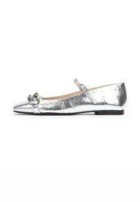 Bailarina metálica plateada con punta afilada, que presenta una correa, un nudo decorativo en la puntera y un tacón bajo y rectangular. Textura suave.