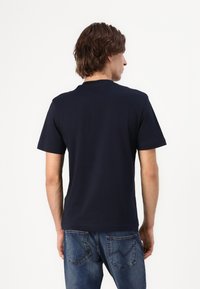 Marineblå bomull t-skjorte med korte ermer, rund hals og rett snitt, kombinert med lyseblå denim jeans. Bakvisning.